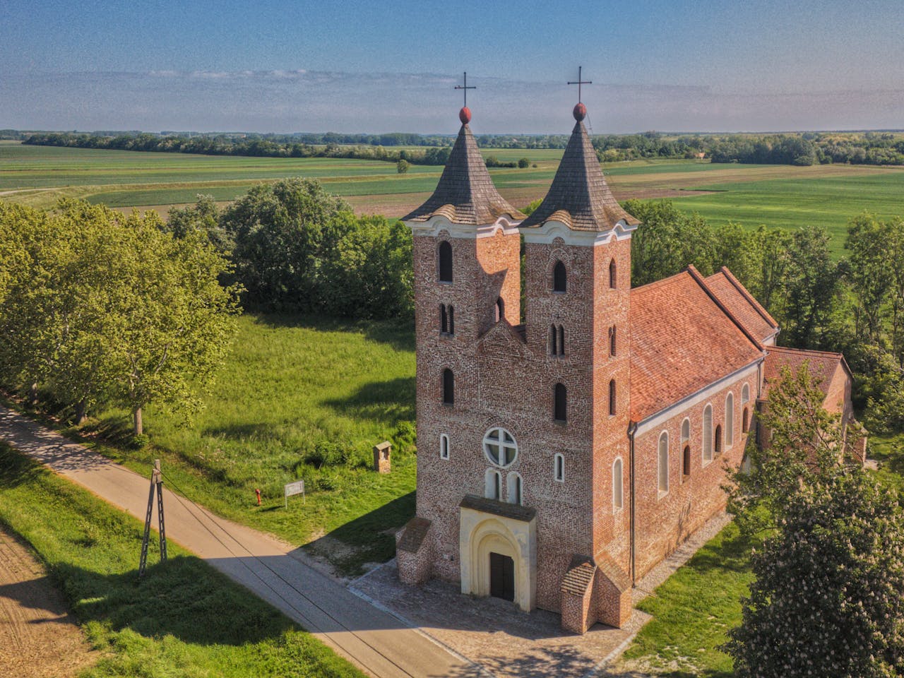 Aerial view of a historical brick church with twin towers in a green rural setting.